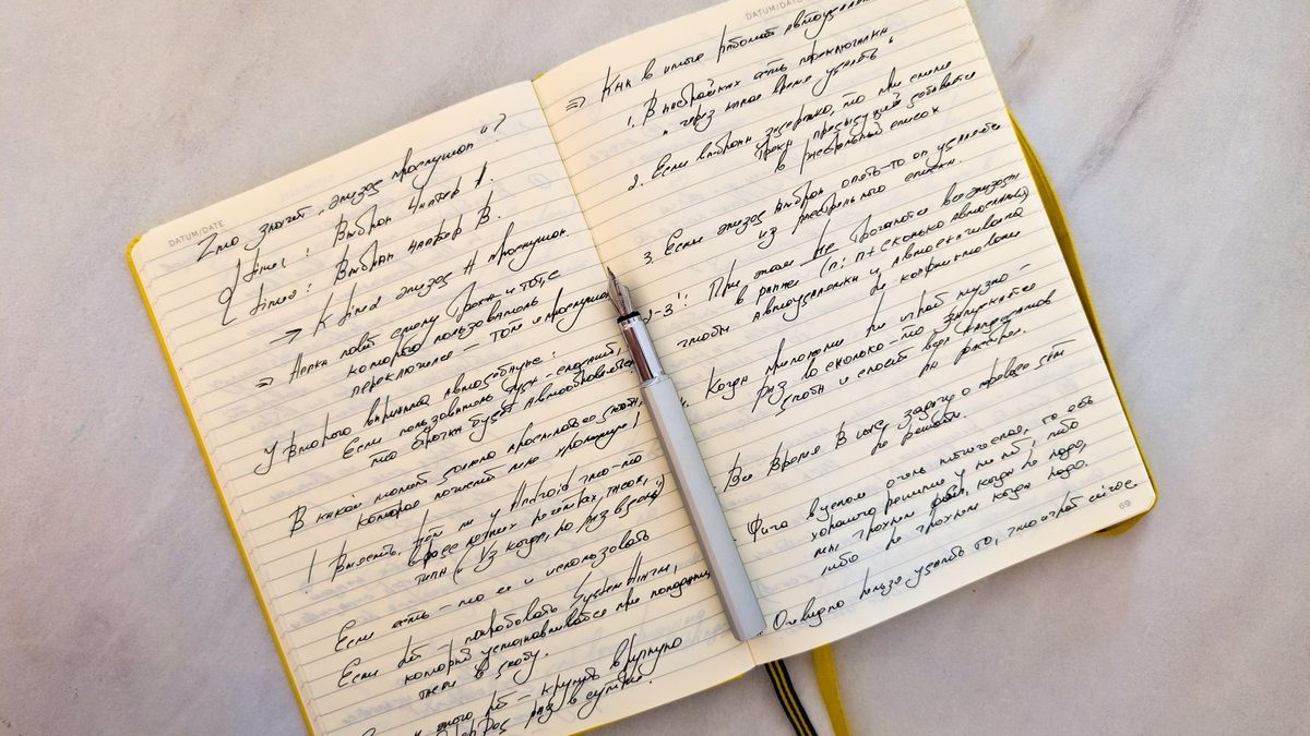 An open notebook with handwritten pages and a pen resting across it